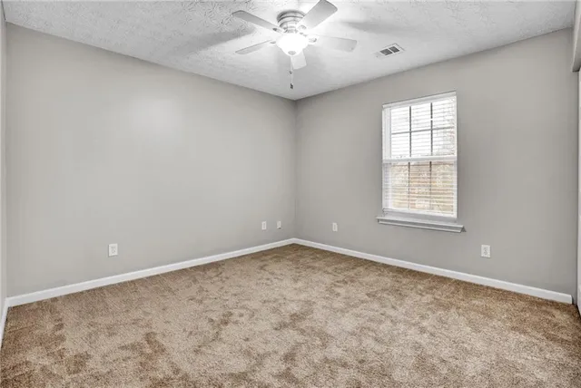 an empty room with chandelier fan and windows