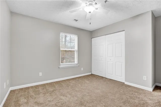 an empty room with chandelier fan and windows