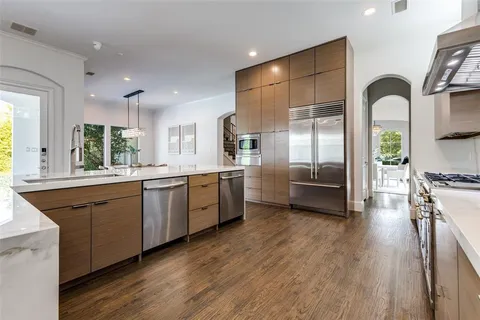 a kitchen with stainless steel appliances kitchen island granite countertop a stove a sink a refrigerator and white cabinets with wooden floor