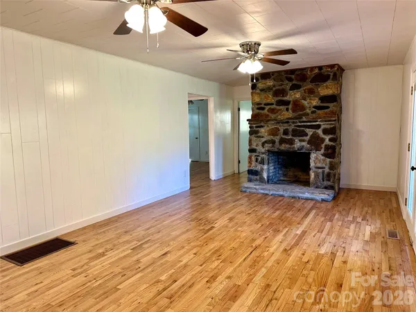 an empty room with wooden floor fireplace and chandelier