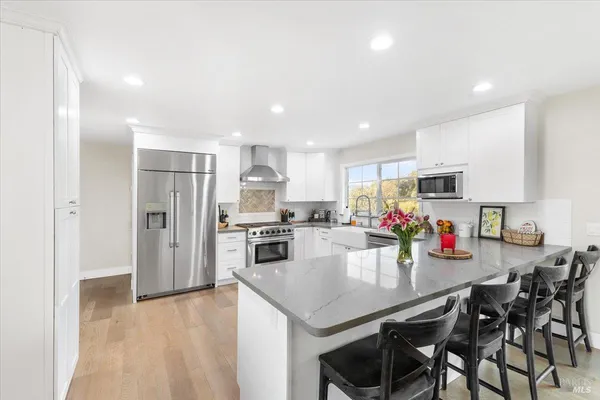 a kitchen with stainless steel appliances kitchen island granite countertop a refrigerator a stove a sink a dining table and chairs with wooden floor