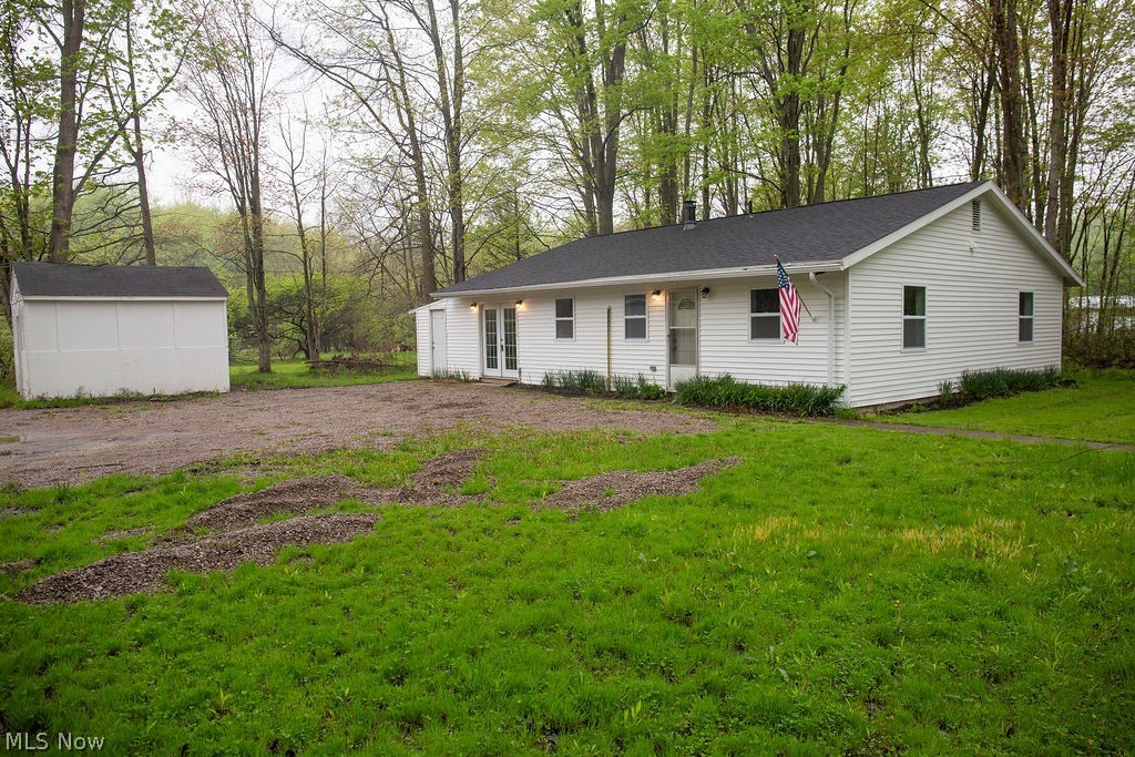 3644 Padanarum Road Geneva, OH 44041 - Photo 2 of 19 White-sided home featuring a black shingle roof, established lawn, ample gravel parking, a detached storage shed, and mature trees surrounding the property