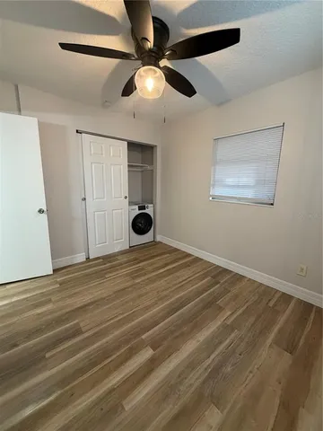 a view of an empty room with wooden floor and a ceiling fan