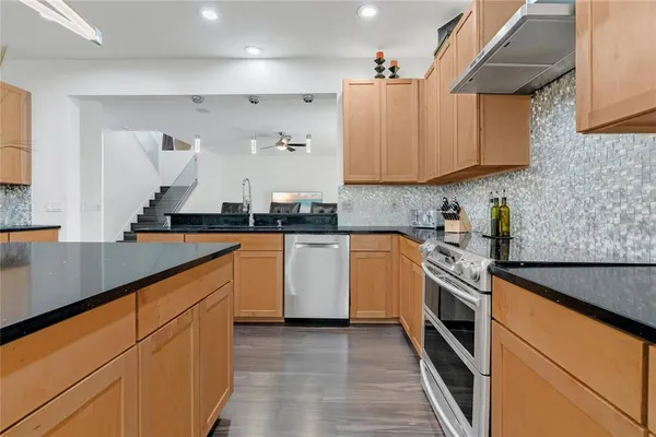 a kitchen with stainless steel appliances granite countertop a refrigerator a sink dishwasher a stove and white countertops with wooden floor