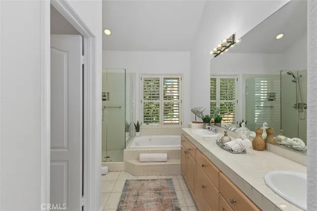 a spacious en suite bathroom with a double vanity sink a large mirror a bathtub and next to a window