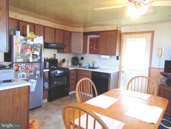 a kitchen with stainless steel appliances kitchen island granite countertop a refrigerator a sink a stove a dining table and chairs with wooden floor
