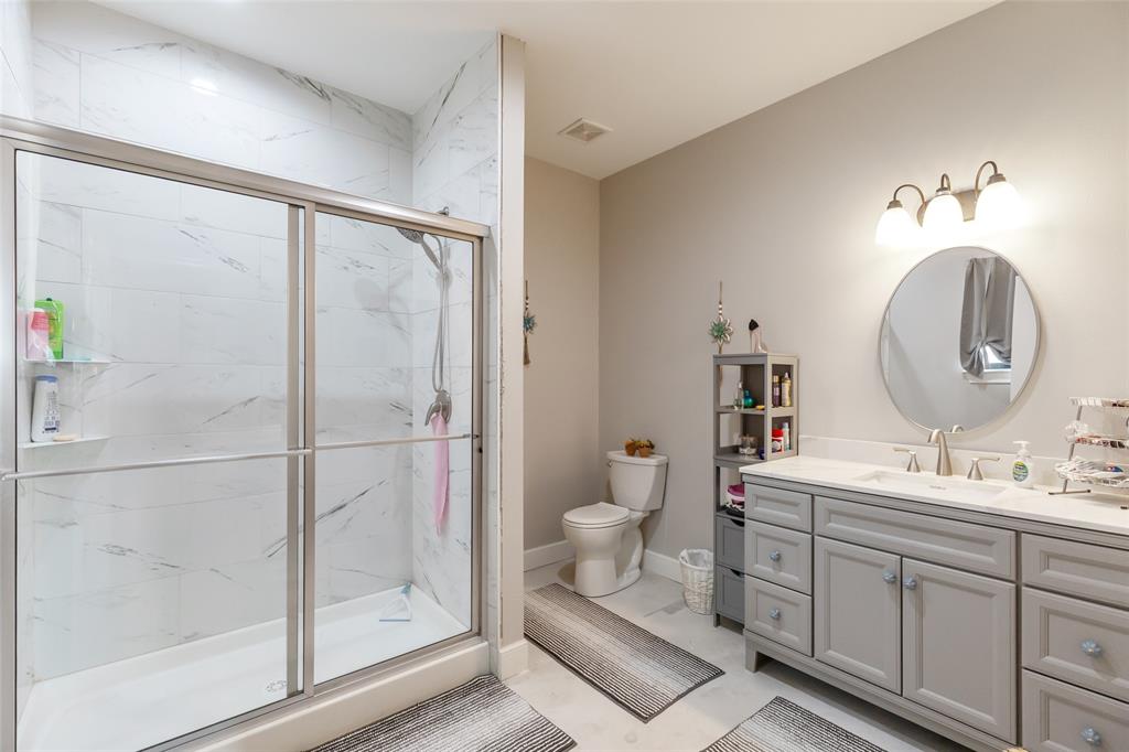760 Wimberly Road Merkel, TX 79536 - Photo 21 of 35 Spacious bathroom featuring a double vanity with light gray cabinetry and white countertops, a round mirror, and a glass-enclosed shower with white tiled walls