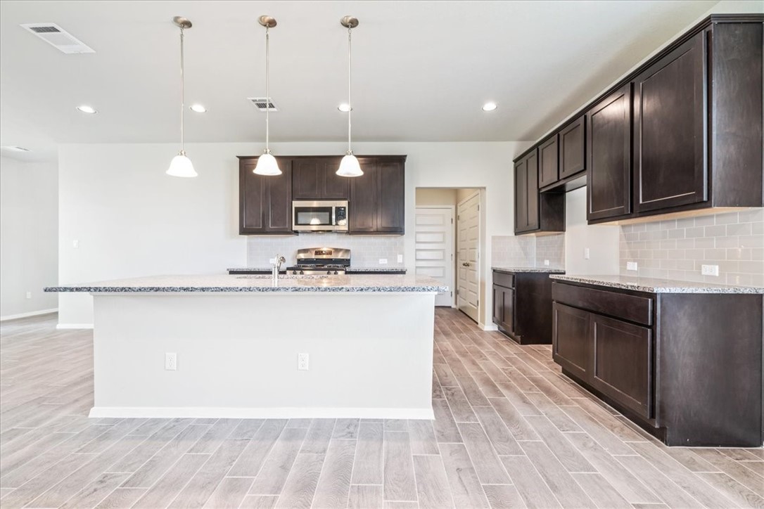 169 Heather Glen Way Maxwell, TX 78656 - Photo 17 of 40 a large kitchen with stainless steel appliances kitchen island granite countertop a stove a sink and a microwave