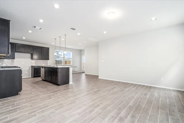 a large kitchen with stainless steel appliances a large counter top a stove a sink dishwasher and a refrigerator with wooden floor