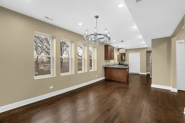 a view of an empty room with wooden floor and a kitchen
