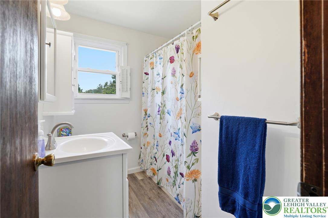 1385 Woodmere Road Pottstown, PA 19464 - Photo 33 of 57 A well-lit full bathroom features a vanity sink, window, and shower area with a vibrant floral curtain.