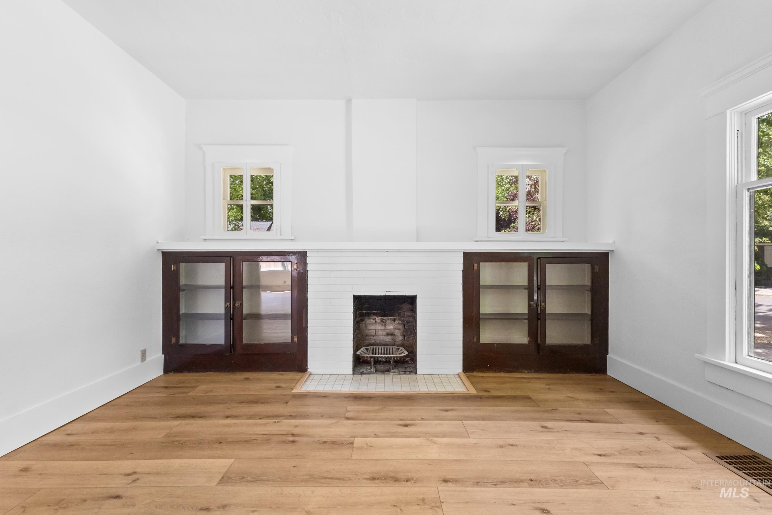 2119 West Brumback Street Boise, ID 83702 - Photo 10 of 30 Living area featuring a white brick fireplace with a tile hearth, flanked by built-in cabinetry with glass panel doors