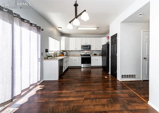 a kitchen with stainless steel appliances granite countertop a refrigerator a sink dishwasher a stove and white countertops with wooden floor