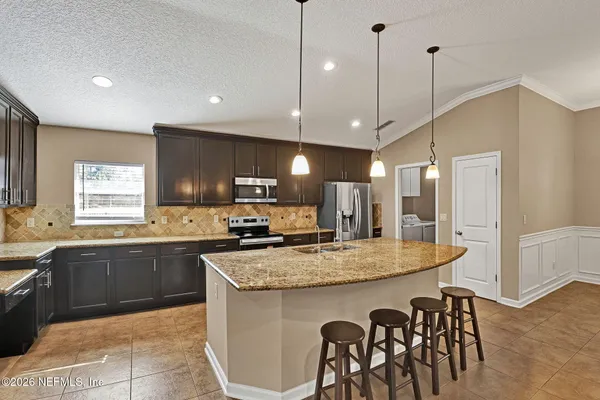 a kitchen with stainless steel appliances granite countertop a kitchen island a stove a table a sink and a refrigerator