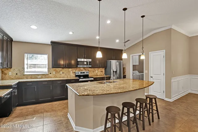 a kitchen with stainless steel appliances granite countertop a kitchen island a stove a table a sink and a refrigerator