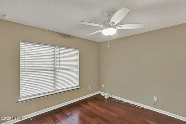 an empty room with wooden floor fan and windows