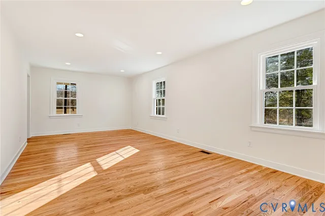 a view of an empty room with wooden floor and kitchen view