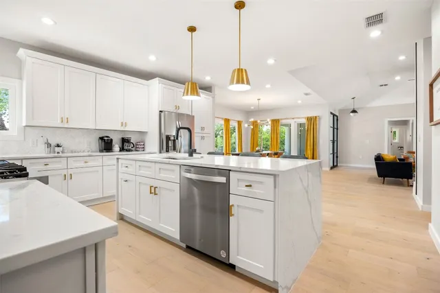 a kitchen with stainless steel appliances kitchen island granite countertop a stove a sink and a view of living room with a window