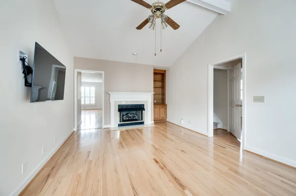 an empty room with wooden floor a ceiling fan a fireplace and windows