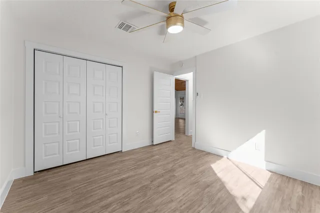 an empty room with wooden floor fan and windows