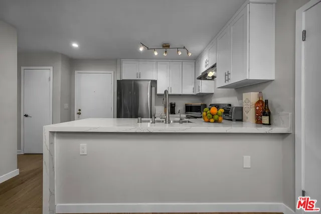 a kitchen with stainless steel appliances granite countertop a refrigerator a sink dishwasher and white cabinets with wooden floor