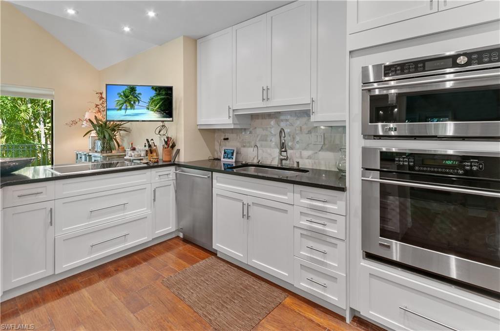1313 Solana Road, Unit A3 Naples, FL 34103 - Photo 12 of 29 Kitchen with appliances with stainless steel finishes, lofted ceiling, white cabinets, light wood finished floors, and dark stone counters