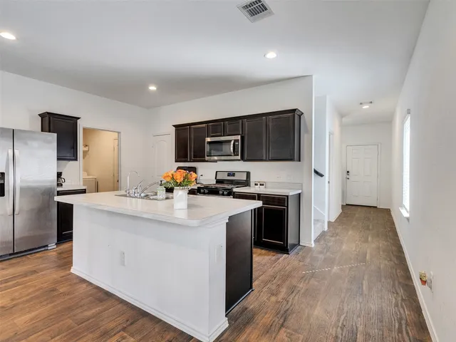 a kitchen with stainless steel appliances a stove top oven a refrigerator a sink and dishwasher with wooden floor