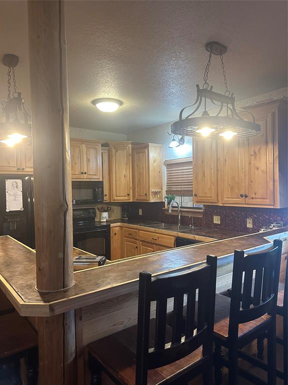 572 Oak Point Drive May, TX 76857 - Photo 15 of 36 Kitchen featuring stove, light brown cabinets, a kitchen bar, dark countertops, and a textured ceiling