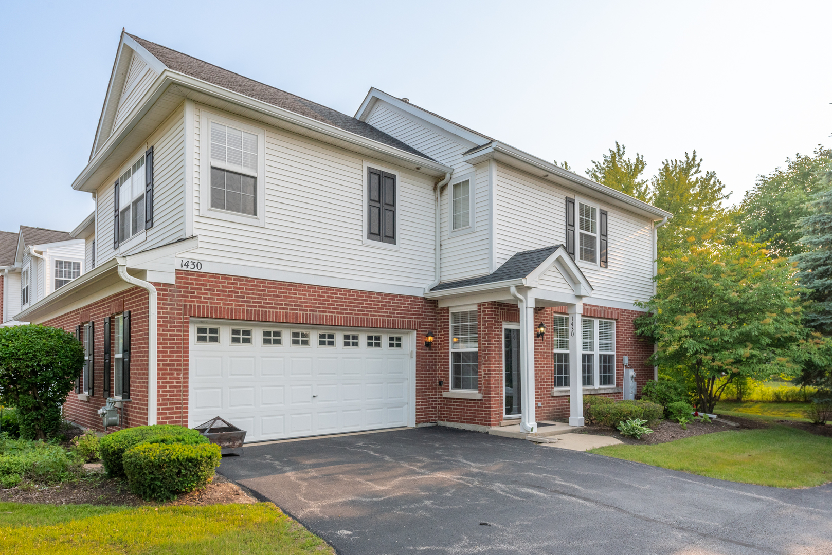 a view of a white house with a large windows and a yard with plants and large tree