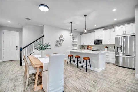 a kitchen with stainless steel appliances granite countertop a refrigerator a stove top oven a dining table and chairs with wooden floor