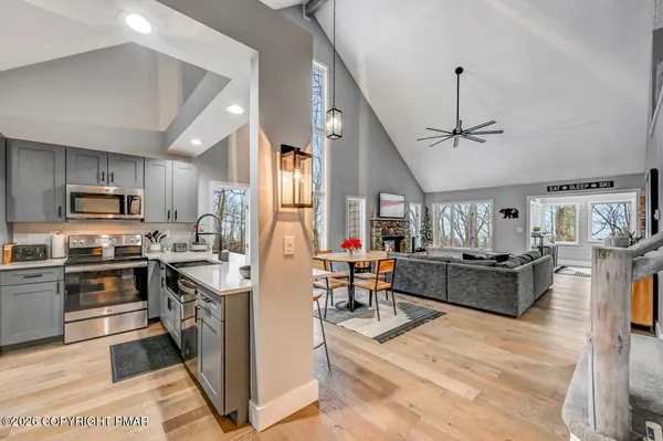a living room with stainless steel appliances kitchen island granite countertop a stove top oven a sink dishwasher a dining table and chairs with wooden floor