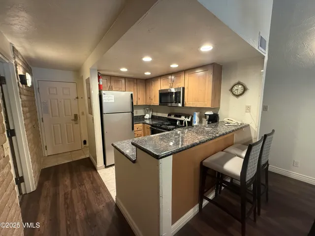 a kitchen with granite countertop a refrigerator a sink a stove a microwave oven and a dining table with wooden floor