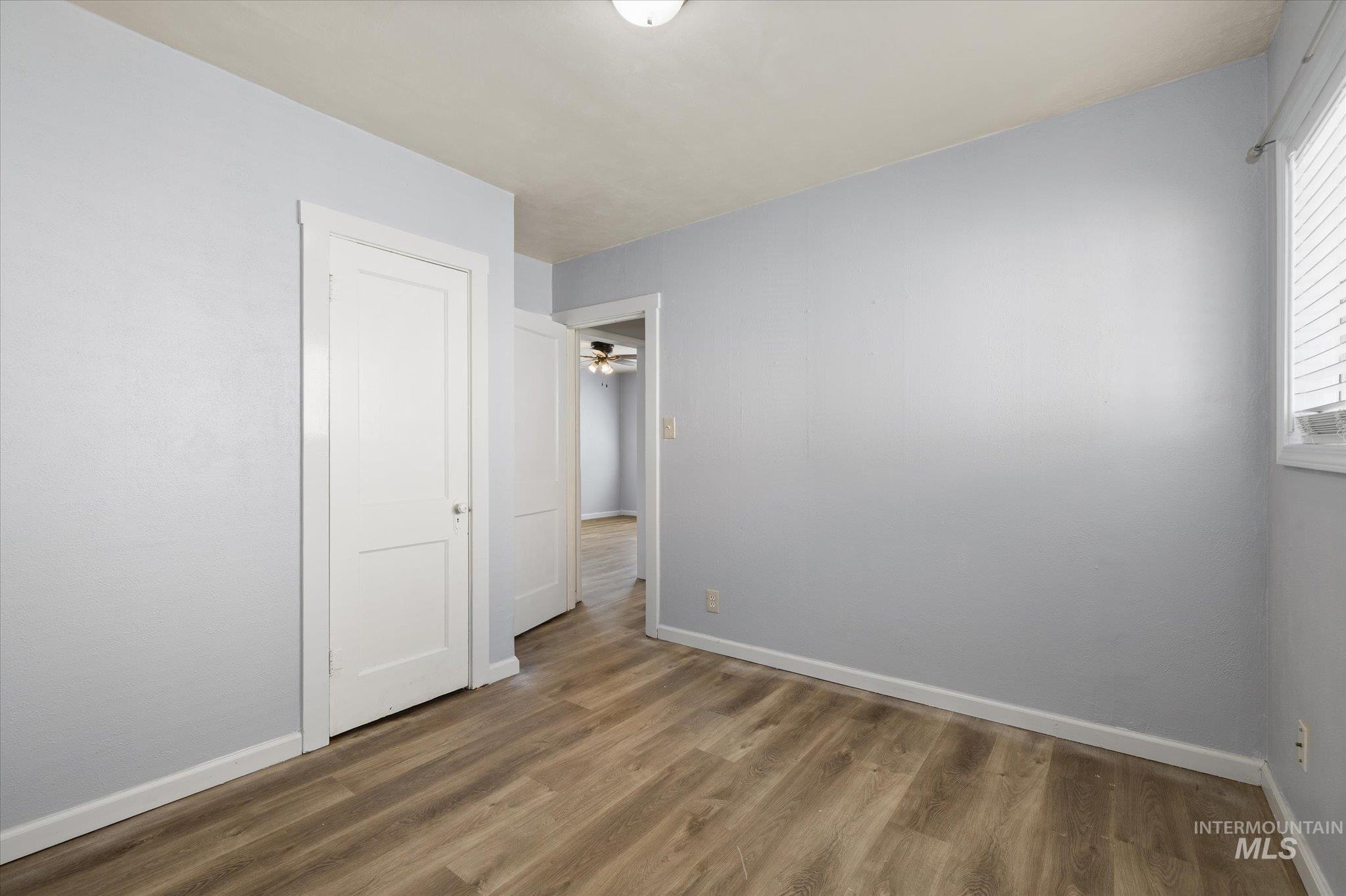 918 West 3rd Street Weiser, ID 83672 - Photo 13 of 36 Room featuring wood-finish flooring, light blue wall paint, white trim, and a window with blinds