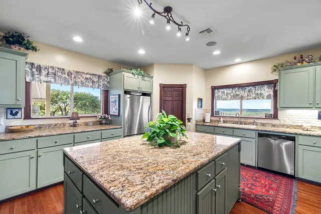 a large kitchen with stainless steel appliances kitchen island granite countertop a large kitchen island a stove a refrigerator a sink dishwasher and wooden cabinets with wooden floor