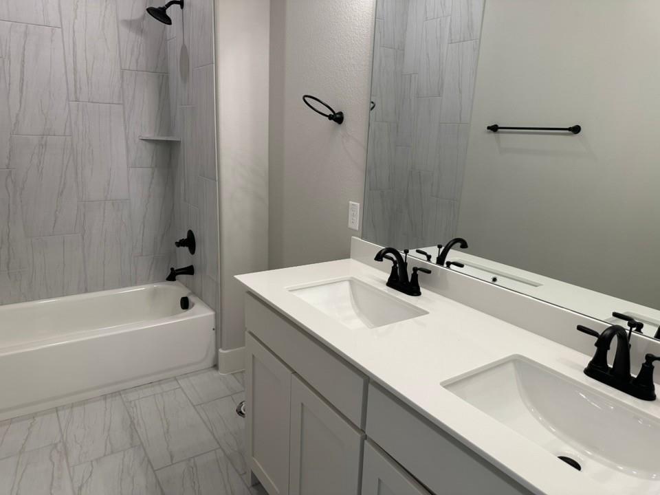 390 Cobb Road Leonard, TX 75452 - Photo 20 of 26 Bathroom featuring a dual vanity with white countertops and integrated sinks, matte black fixtures, a full-width mirror, a tub-shower combination with light-toned rectangular wall tiling, and coordinating floor tiling