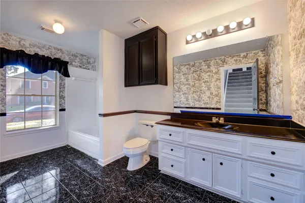 a bathroom with a granite countertop toilet a sink and a window