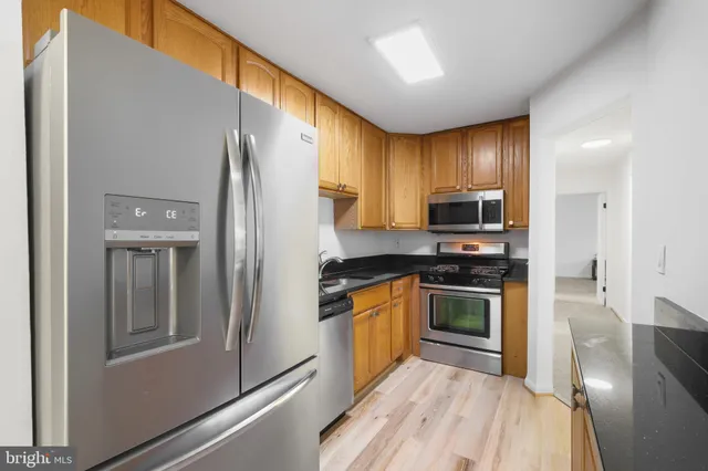 a kitchen with stainless steel appliances granite countertop a refrigerator a stove and a sink with wooden floor