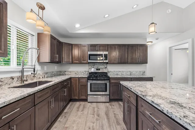 a kitchen with stainless steel appliances granite countertop a sink a stove a refrigerator and a oven with wooden floor