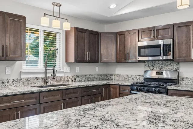 a large kitchen with stainless steel appliances granite countertop a refrigerator a stove a sink and a microwave