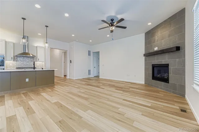 a view of an empty room and kitchen with fireplace ceiling fan