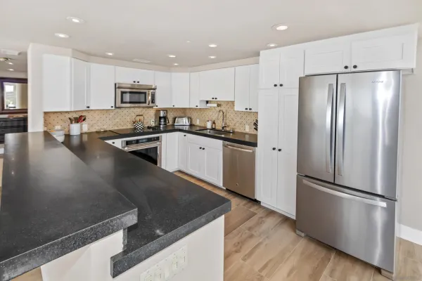 a kitchen with stainless steel appliances granite countertop a refrigerator a sink a stove and white cabinets with wooden floor