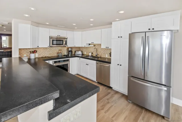 a kitchen with stainless steel appliances granite countertop a refrigerator a sink a stove and white cabinets with wooden floor