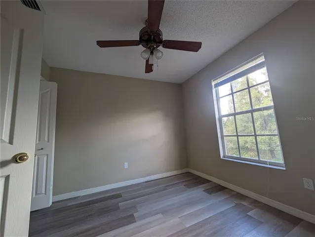 an empty room with wooden floor fan and windows