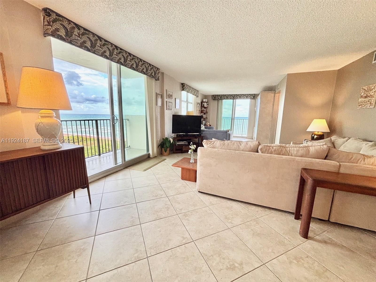 9273 Collins Avenue, Unit 705 Surfside, FL 33154 - Photo 22 of 40 a living room with couches a flat screen tv and kitchen view