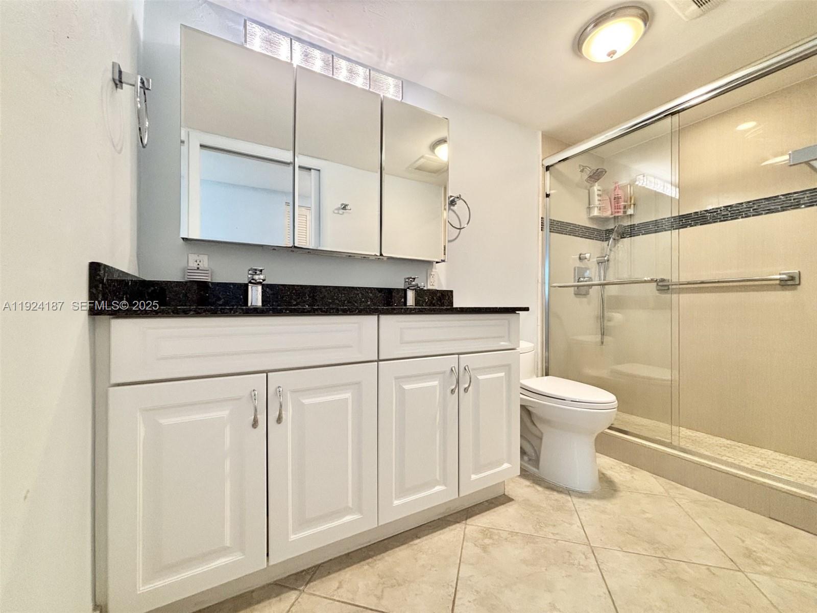 9273 Collins Avenue, Unit 705 Surfside, FL 33154 - Photo 32 of 40 a bathroom with a granite countertop sink a toilet and a mirror