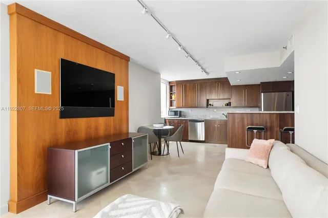 a living room with stainless steel appliances furniture a flat screen tv and kitchen view