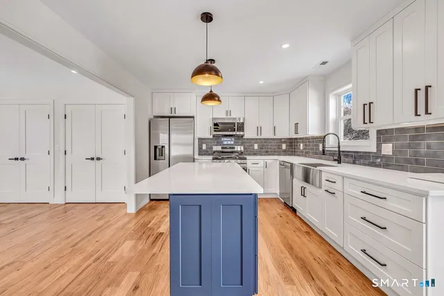 a kitchen with stainless steel appliances granite countertop a sink dishwasher a stove and white cabinets with wooden floor