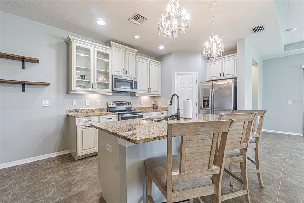 4256 Ashton Meadows Way Wesley Chapel, FL 33543 - Photo 4 of 42 a kitchen with stainless steel appliances granite countertop a stove top oven a refrigerator a sink and a dining table with wooden floor