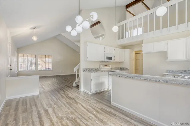 a large kitchen with granite countertop a stove a sink and white cabinets with wooden floor