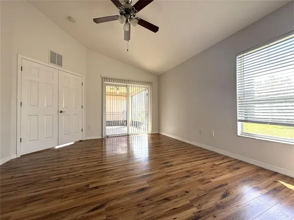 an empty room with wooden floor fan and windows